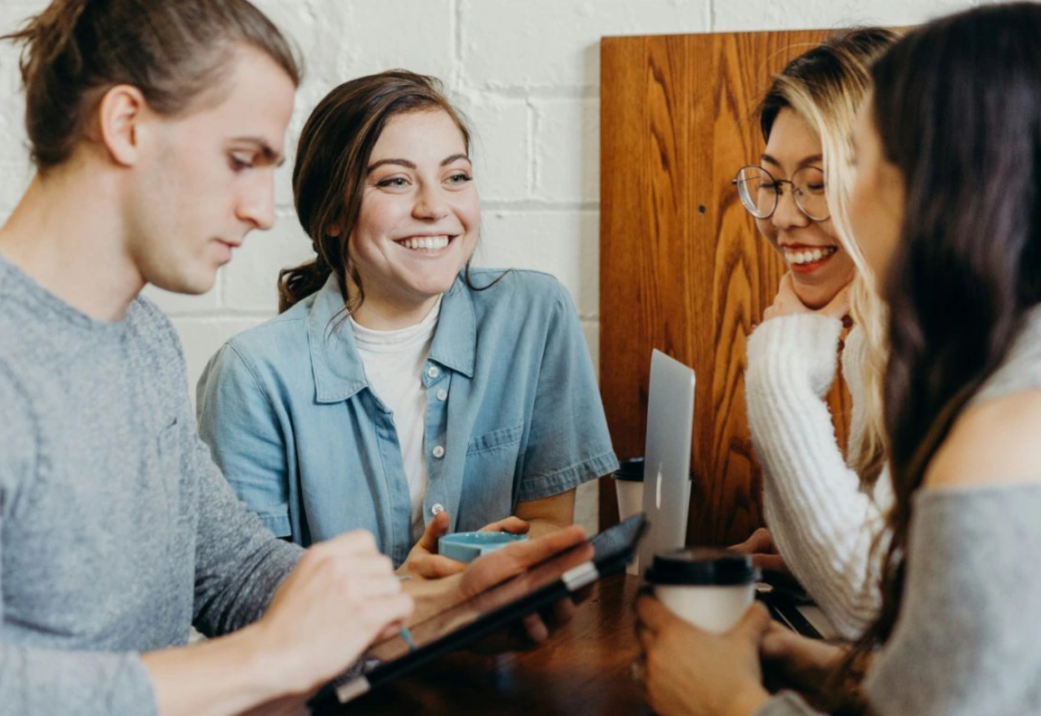 Drie vrouwen en een man zitten lachend aan een tafel in overleg.