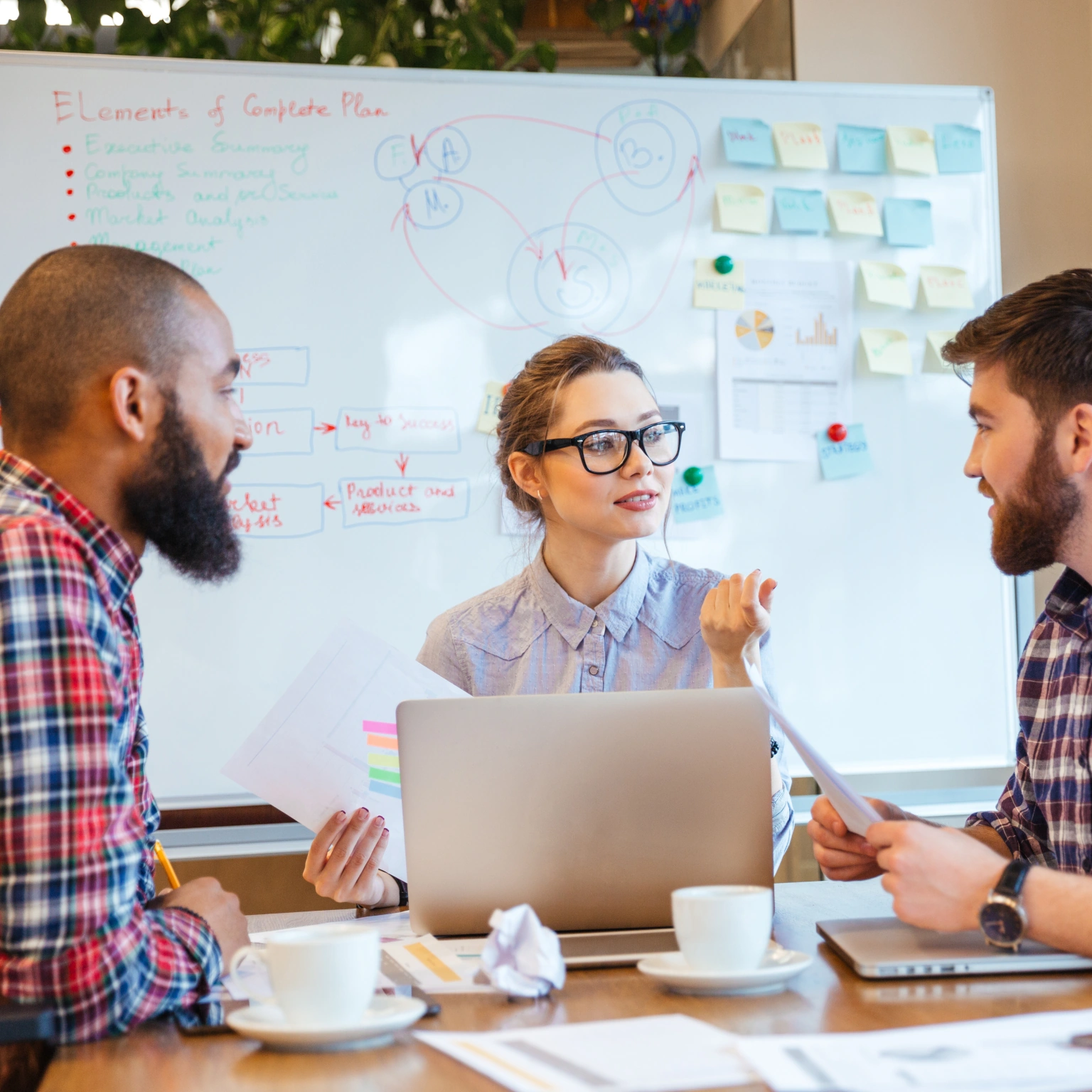 Drie mensen in overleg achter een bureau voor een whiteboard.