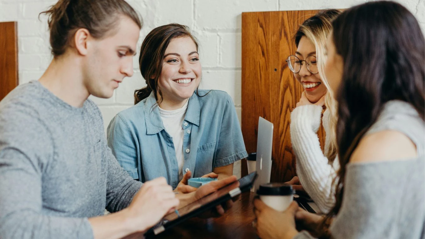 Drie vrouwen en een man zitten lachend aan een tafel in overleg.