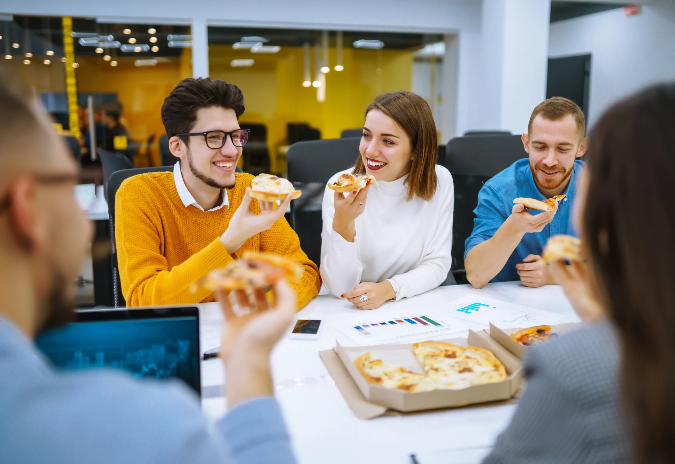 Gezellig team eet tijdens het werk aan tafel een pizza.